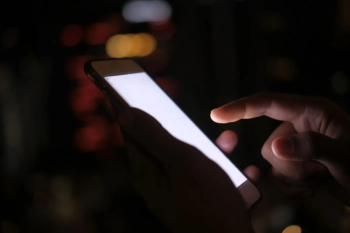A hand holding a phone against city lights at night (stock photo)