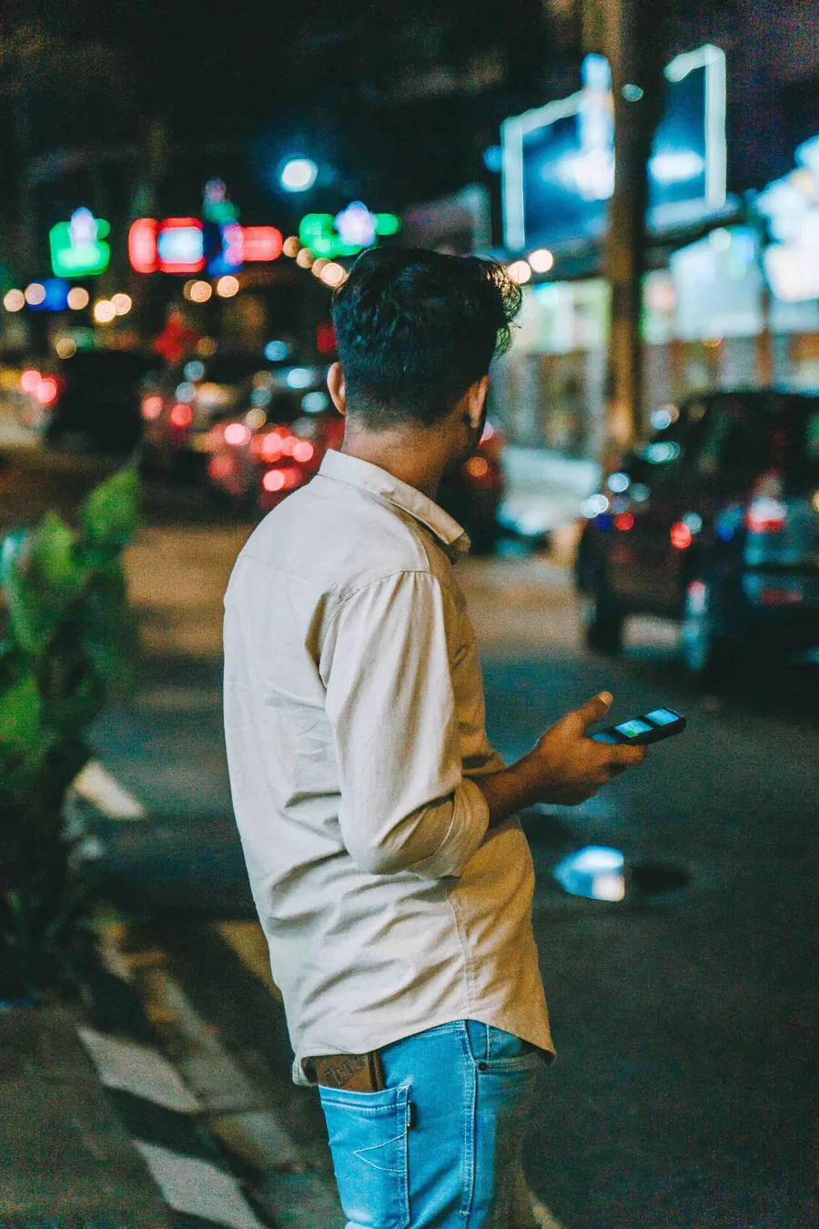 A man checking his phone on a Kuala Lumpur street at night, seen from behind (stock photo)
